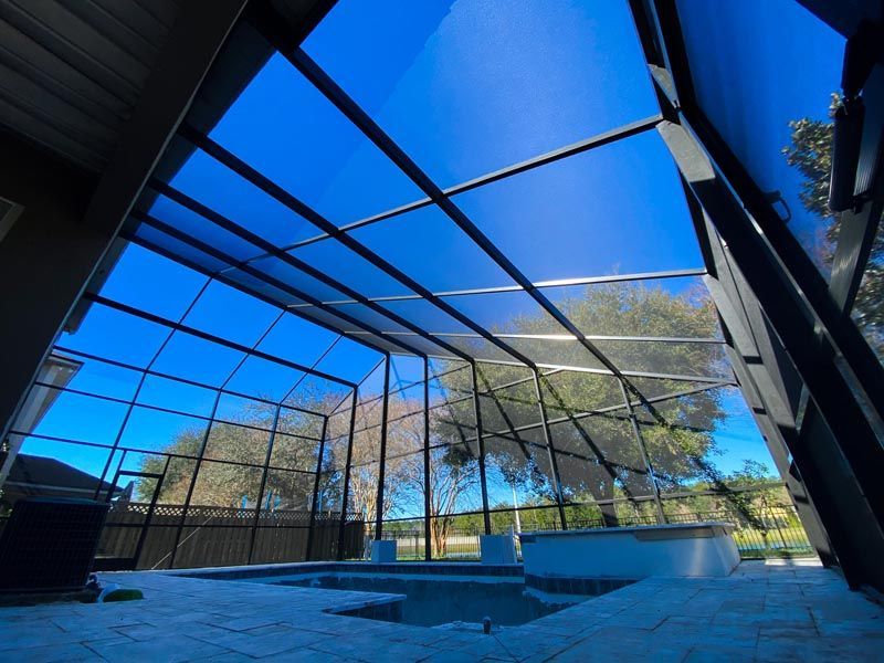 Covered outdoor pool beneath a glass roof, with blue sky and trees visible through the enclosure