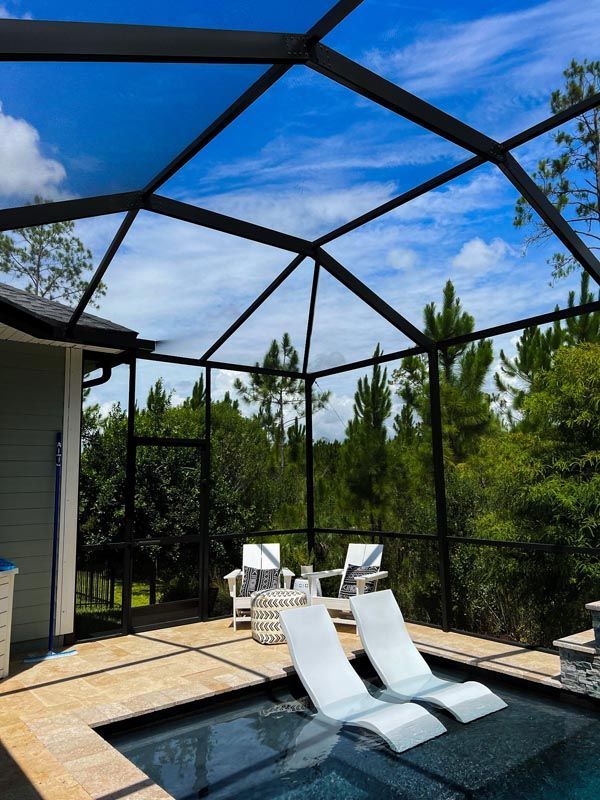 Screened backyard pool with white loungers under a blue sky and trees beyond the fence