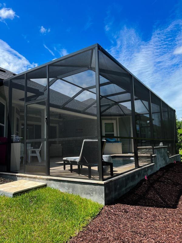 Screened patio with black frame, patio furniture, and pool under a bright blue sky