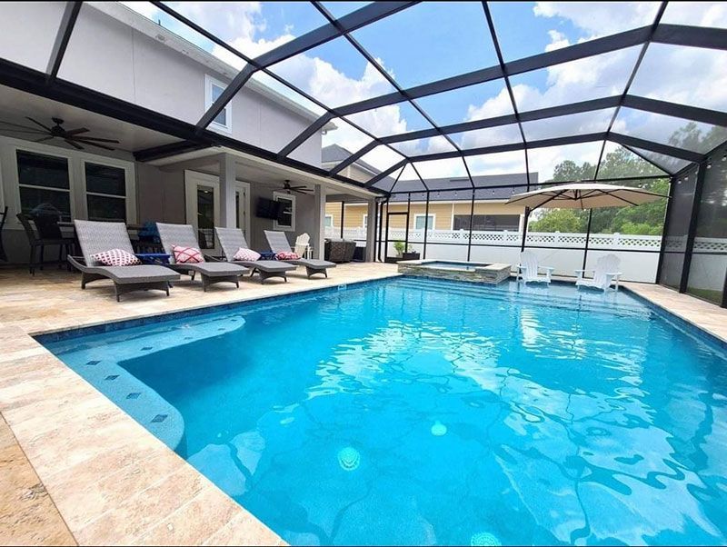 Covered outdoor swimming pool with lounge chairs and a screened ceiling