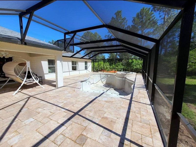 Covered screened patio with tiled floor and empty pool, viewed through black frame under a blue sky