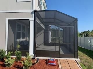 Screened patio attached to a house, with potted plants and mulch in the yard.
