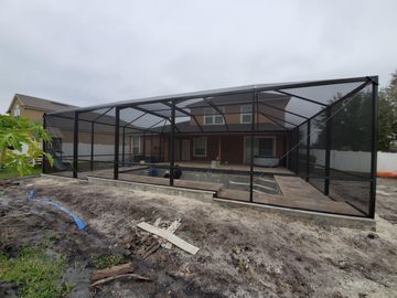 Black metal screened patio enclosure in front of a house under construction