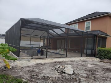 Large screened patio enclosure attached to a house, with a concrete yard and banana plants in front.