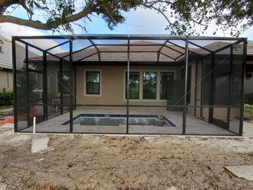 Screened-in patio enclosure around a backyard pool, with black framing and beige house exterior.