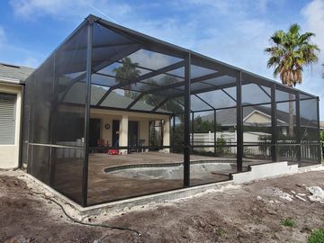 Screened patio enclosure beside a house, with black framing and mesh panels on a concrete slab.