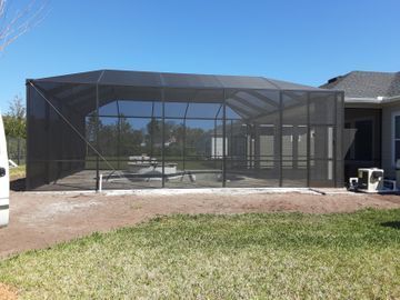Screened-in backyard patio beside a house, with black mesh enclosure and concrete floor