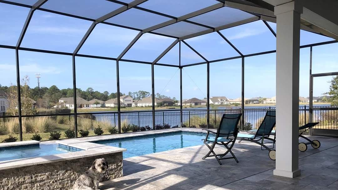 Screened pool patio with lounge chairs overlooking water and houses