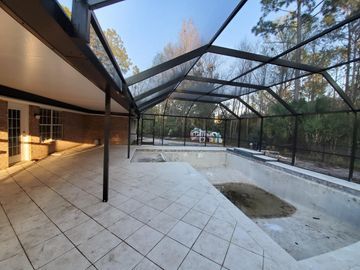 Covered outdoor patio with tiled floor, screened roof, and a fenced pool area in the background