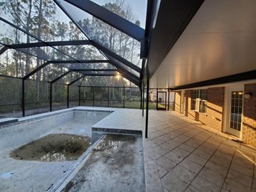 Empty screened-in patio with a tiled pool, concrete deck, and brick house exterior at sunset