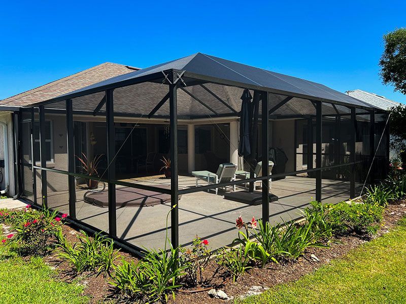 Screened patio with black frame, patio furniture, and a landscaped yard under a bright blue sky