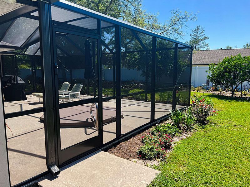 Screened patio enclosure beside a pool with chairs, concrete deck, and landscaped yard