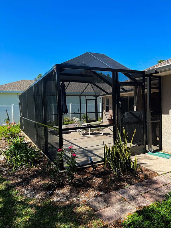 Black screened patio enclosure with a paved floor and plants in a sunny backyard