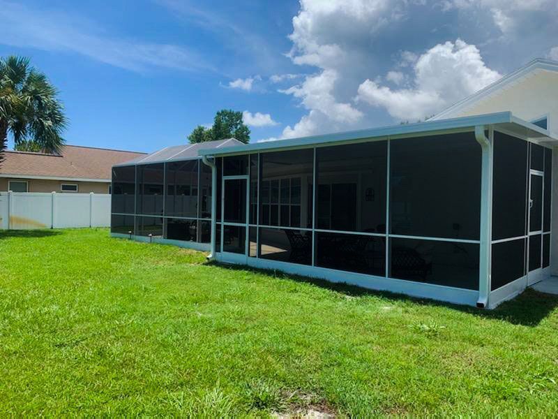 Screened patio enclosure attached to a house, sitting beside a green lawn under a blue sky