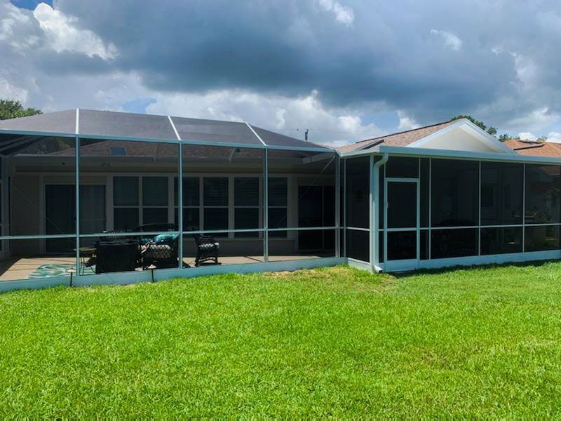 Single-story house with screened porch and green lawn under a cloudy sky