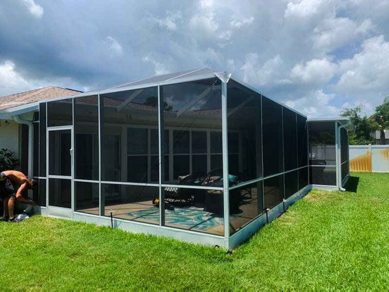 Screened patio enclosure beside a house with a person working on the left and a cloudy sky overhead