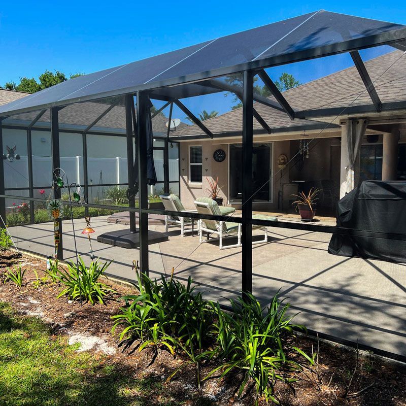 Screened-in patio with outdoor seating and grill beside a house on a sunny day