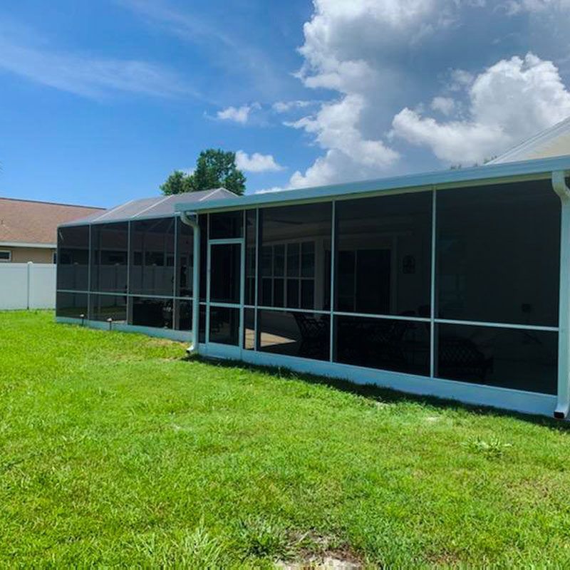 Screened-in patio enclosure with dark mesh panels beside a grassy yard under a blue sky