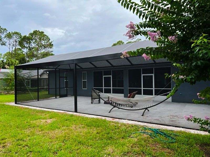 Modern screened patio beside a black house, with a hammock and green lawn under a cloudy sky