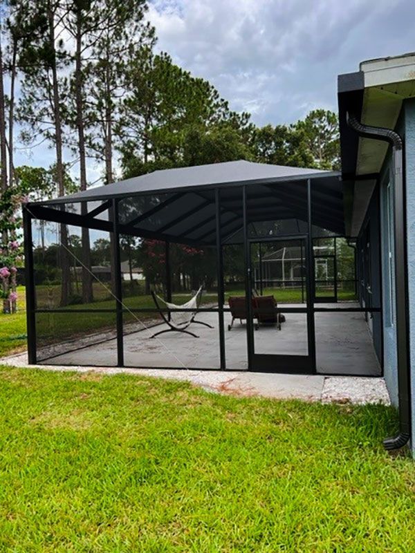 Screened patio enclosure with black frame and gray roof in a grassy backyard
