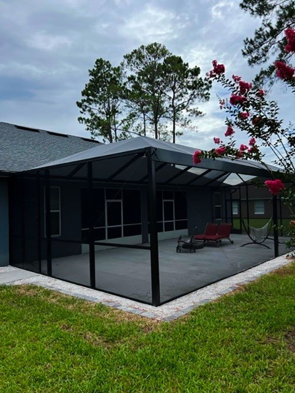 Screened patio beside a dark house, with red patio chairs and trees in the background.