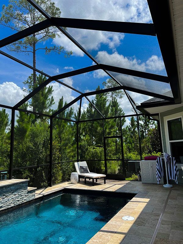 Backyard pool under a screened enclosure with lounge chair, patio, and blue sky above
