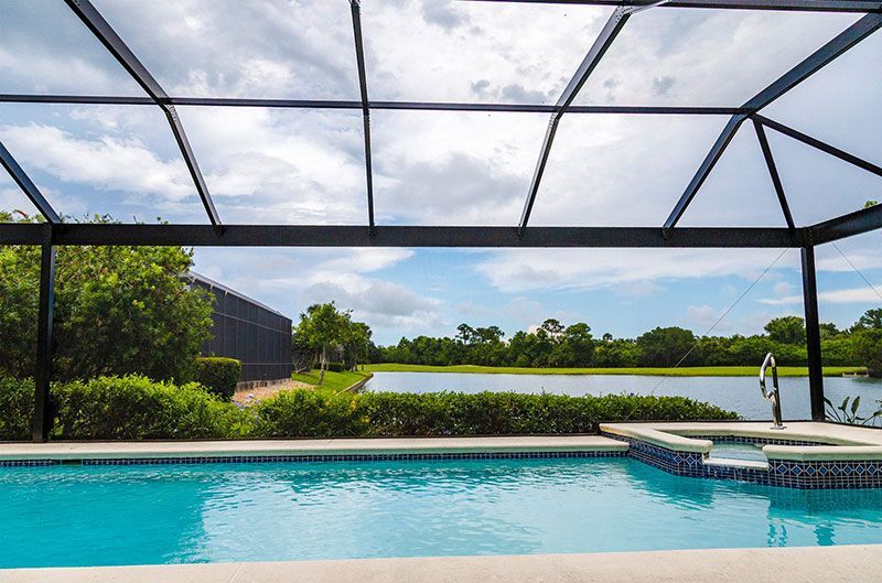 Screened-in pool patio with turquoise water, lake view, and cloudy sky beyond the lanai.