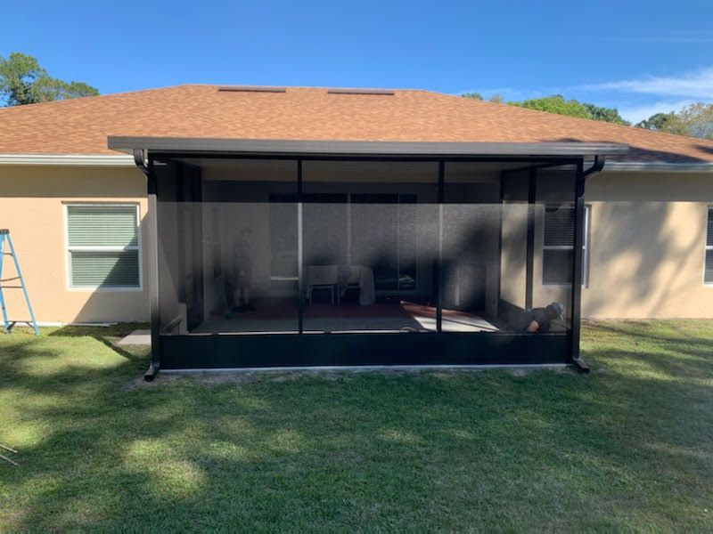 Screened patio enclosure attached to a beige house with a tan roof and green lawn.