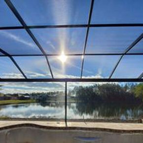 Sunlit lake view through a screened patio enclosure with blue sky and clouds