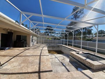 Screened backyard patio with a rectangular pool under construction beside a house