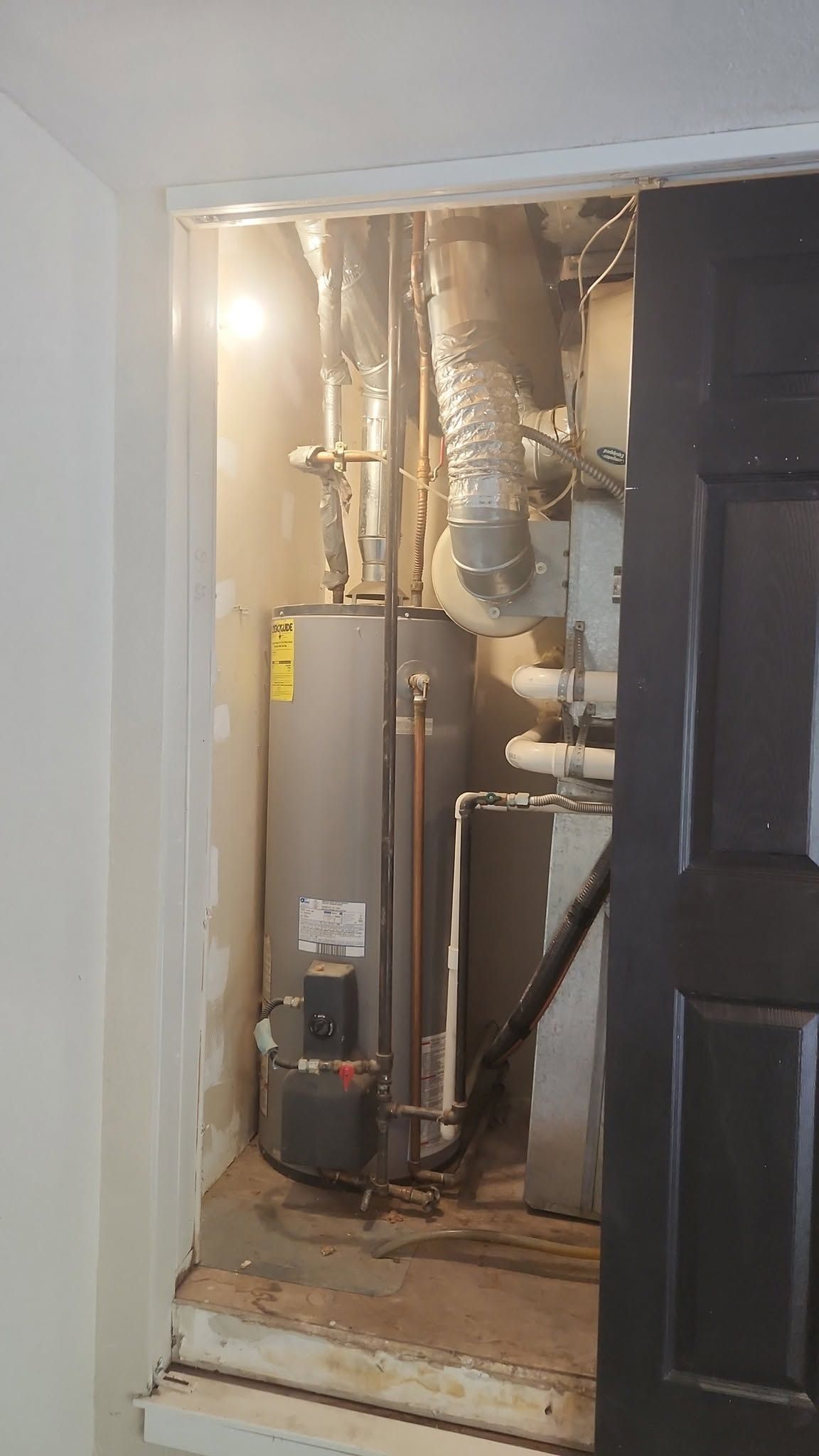 Basement utility closet with water heater, furnace, and exposed pipes next to a black door