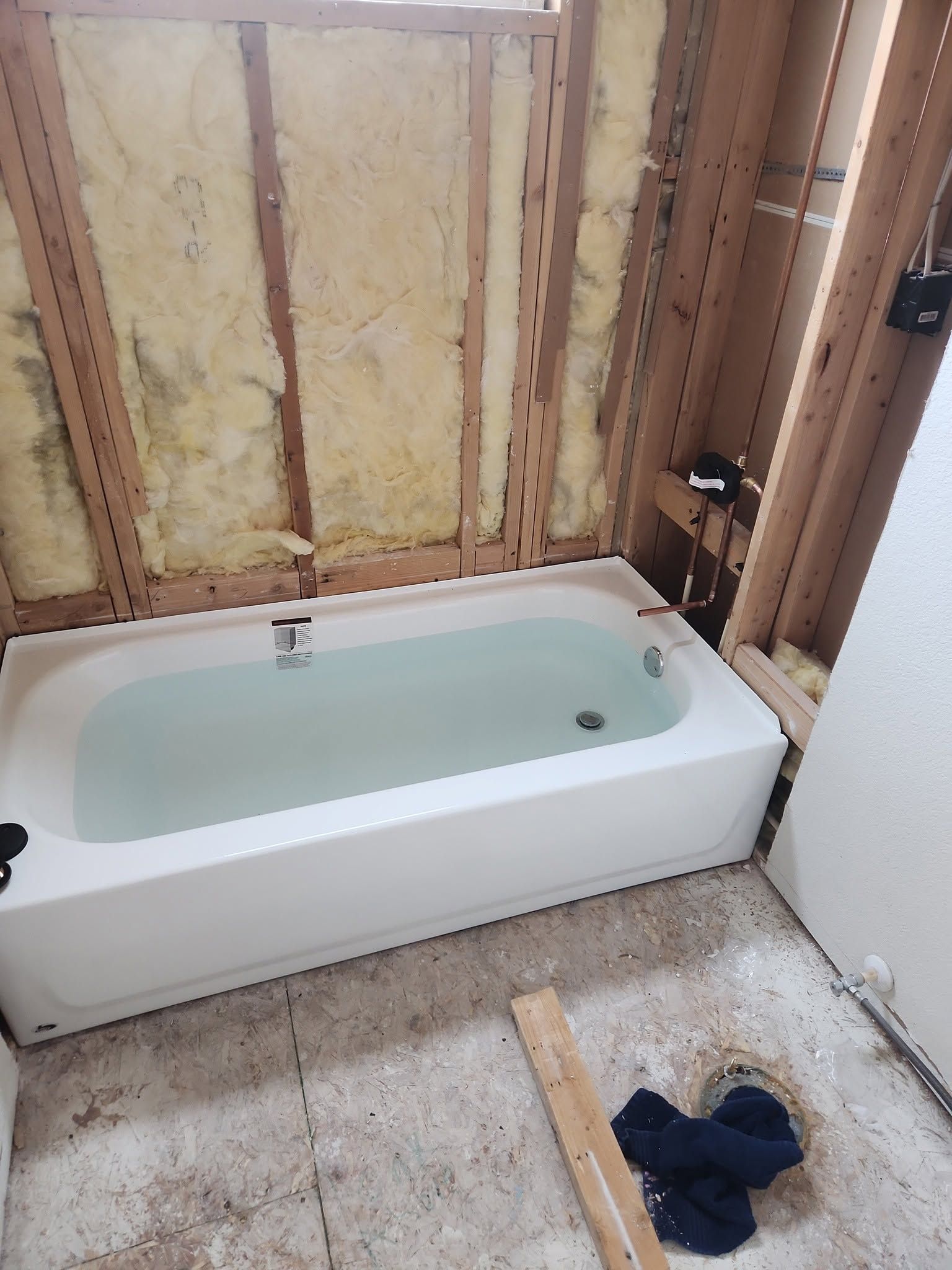 Bathtub in a bathroom under renovation, with exposed insulation and unfinished walls.