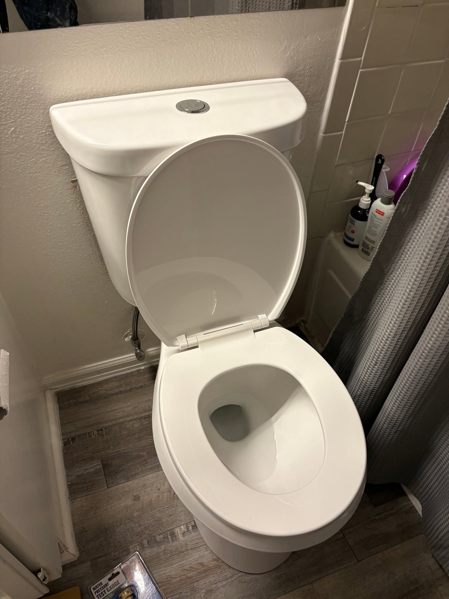 Open toilet in a small bathroom with gray tiles and a shower curtain.