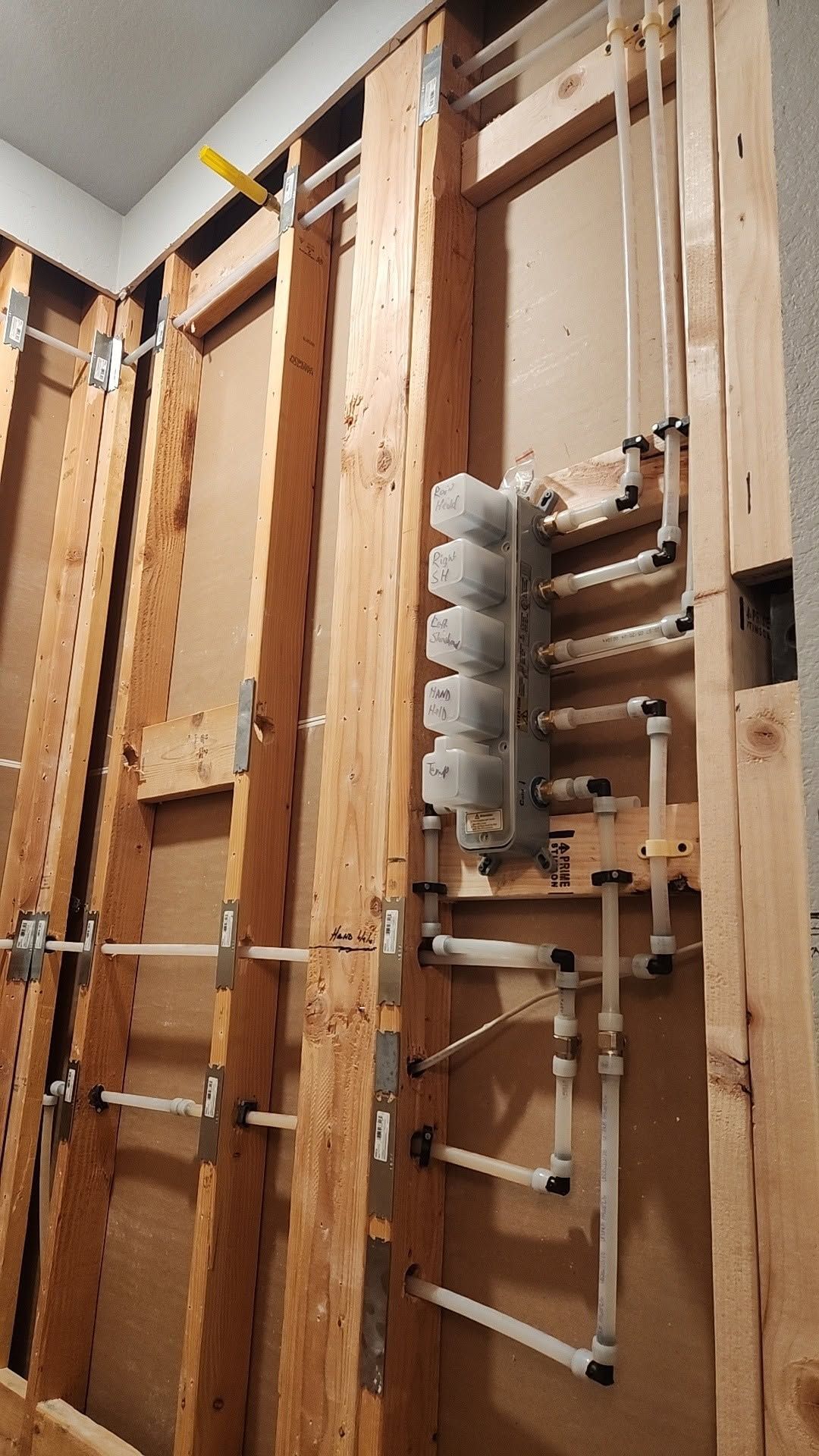 Electrical wiring and pipes installed in unfinished wall framing inside a construction site.