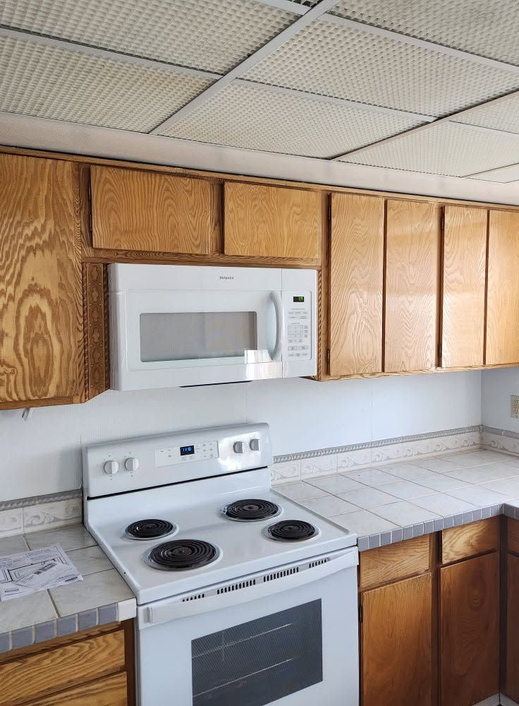 Small kitchen with white stove and microwave beneath wood cabinets and a tiled countertop.