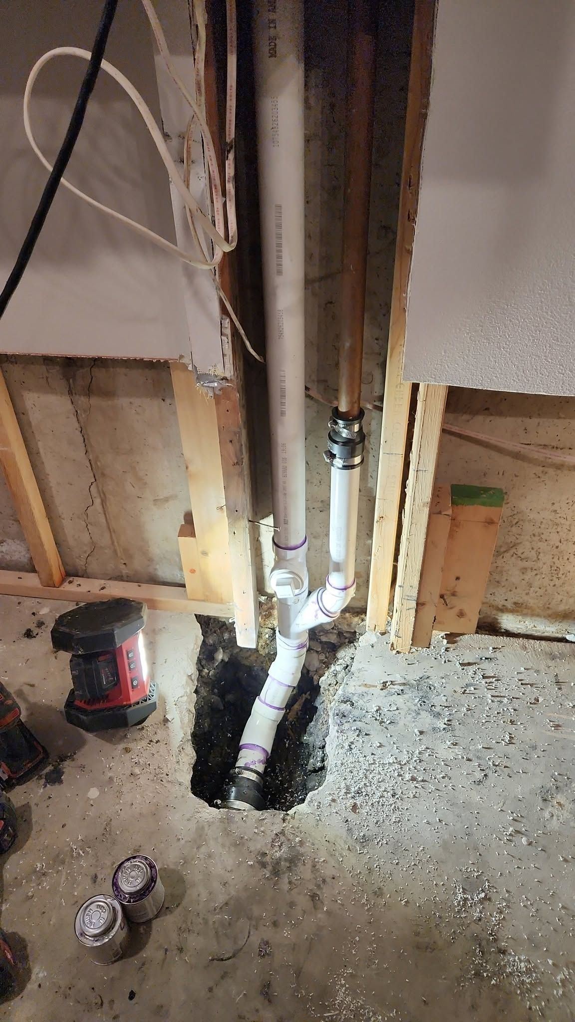 Damaged floor around exposed plumbing pipe in an unfinished interior wall