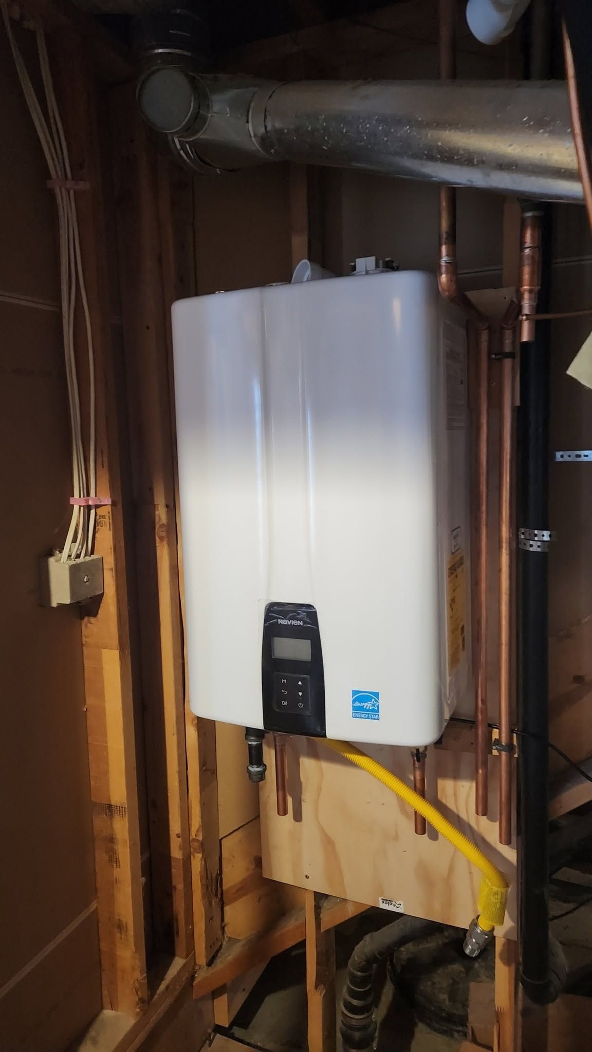 White wall-mounted utility unit in an unfinished basement with exposed pipes and wiring.