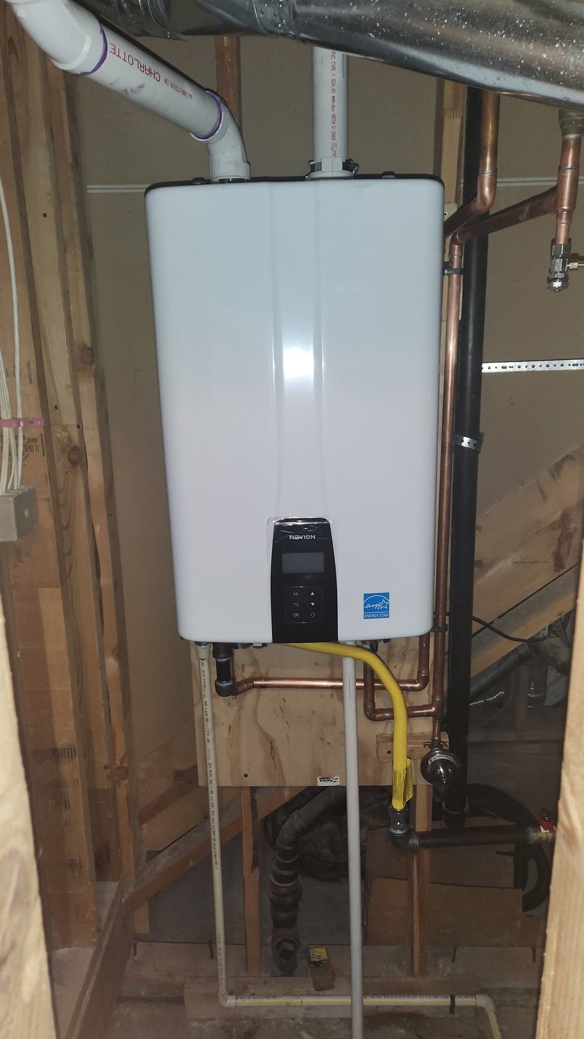 White wall-mounted water heater with pipes in a basement utility area