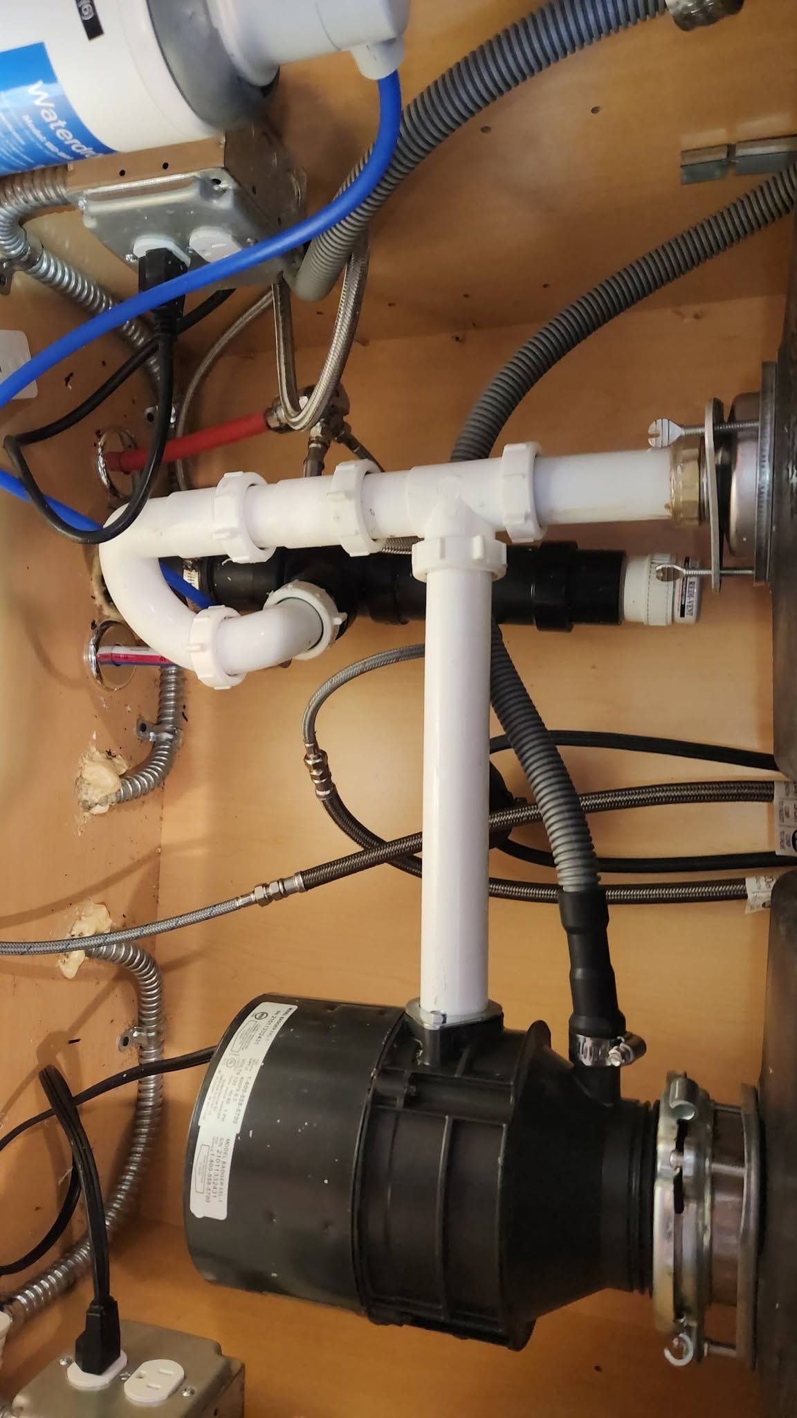 White PVC pipes and black hoses connected to two black pump units in a mechanical compartment