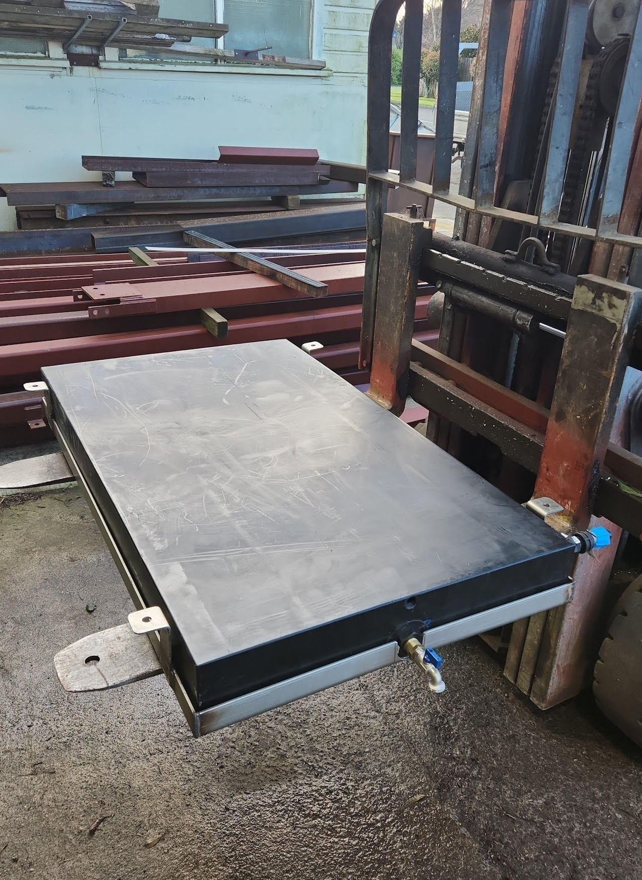 A large piece of metal is sitting on the ground next to a forklift.