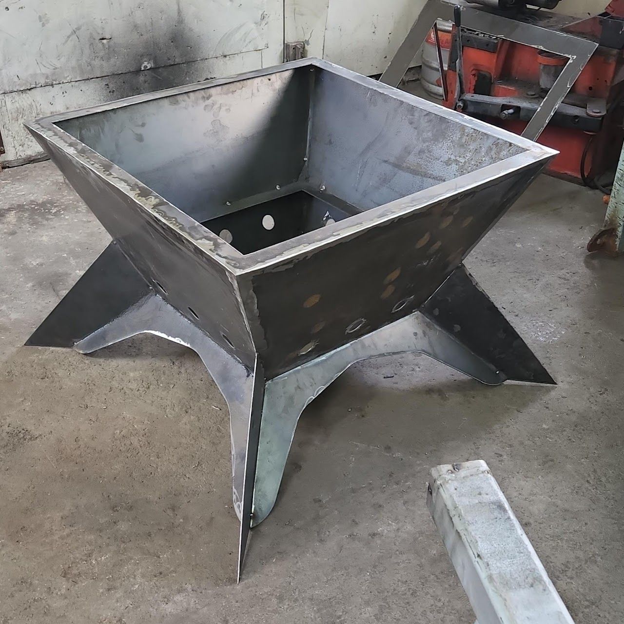 A metal fire pit is sitting on a concrete floor.