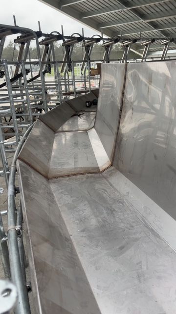 Stainless steel trough with welded seams, likely for agricultural use, under a metal roof.