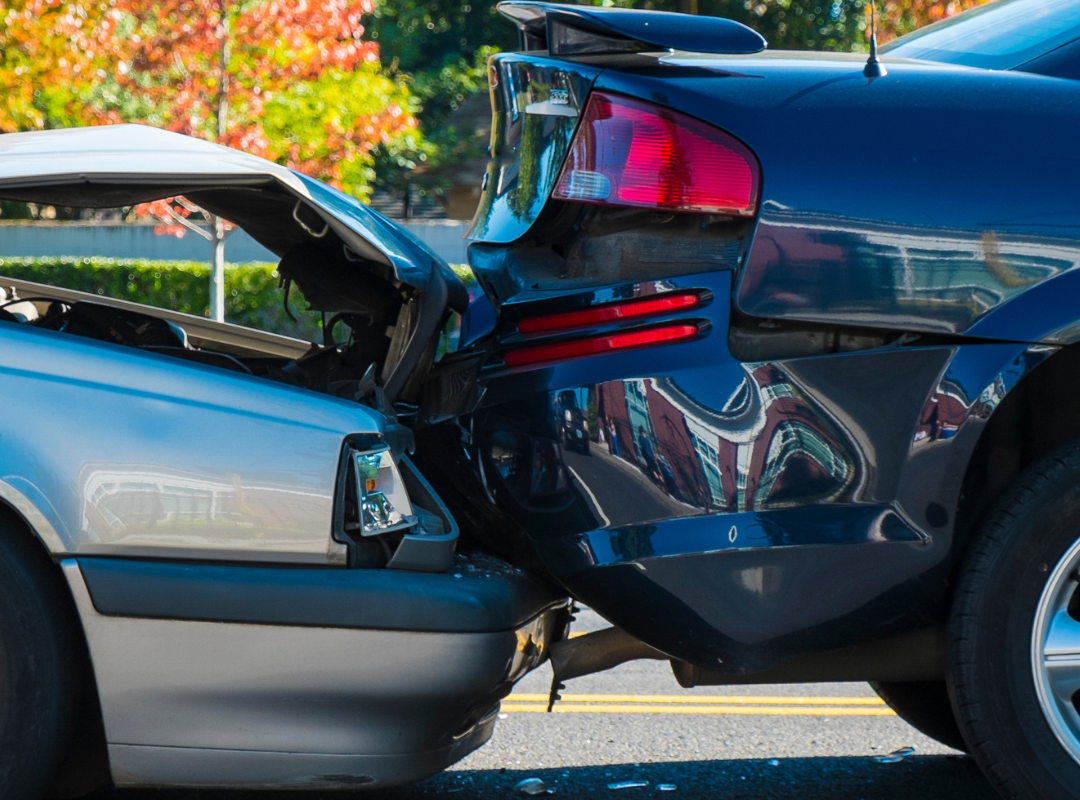 Two cars involved in a rear-end collision on an asphalt road during the day, showing heavy damage to both vehicles.