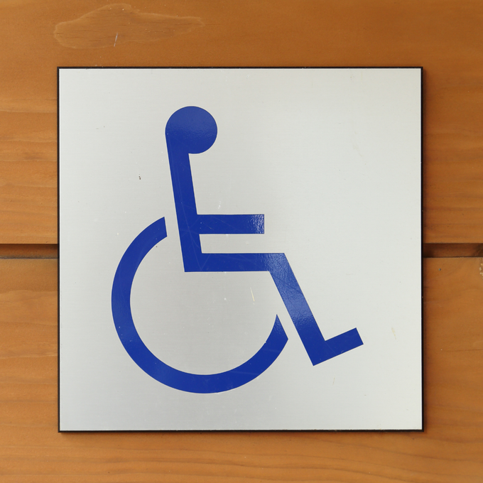A blue International Symbol of Access icon on a square white sign mounted on a wooden wall.