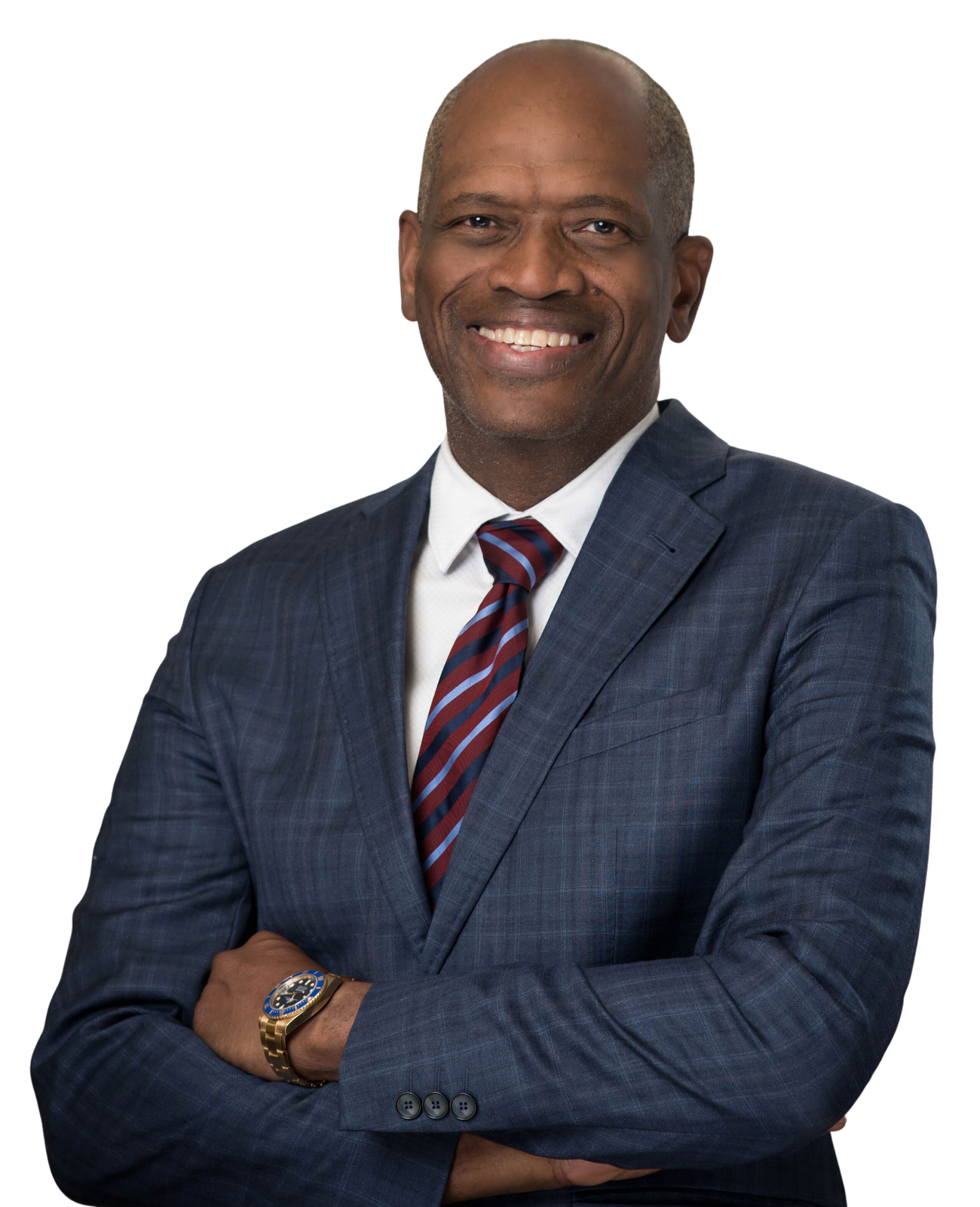 Smiling person wearing a blue plaid suit, white shirt, and striped tie, posing with arms crossed against a white background.