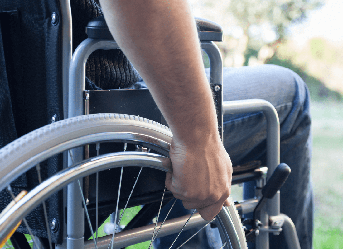 A close-up view of a person's hand gripping the handrim of a manual wheelchair while outdoors.
