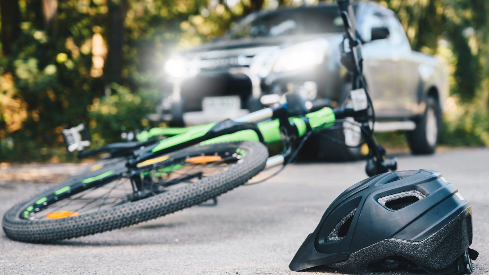A bicycle lies on the road next to a helmet with a blurred car in the background, suggesting a potential accident.