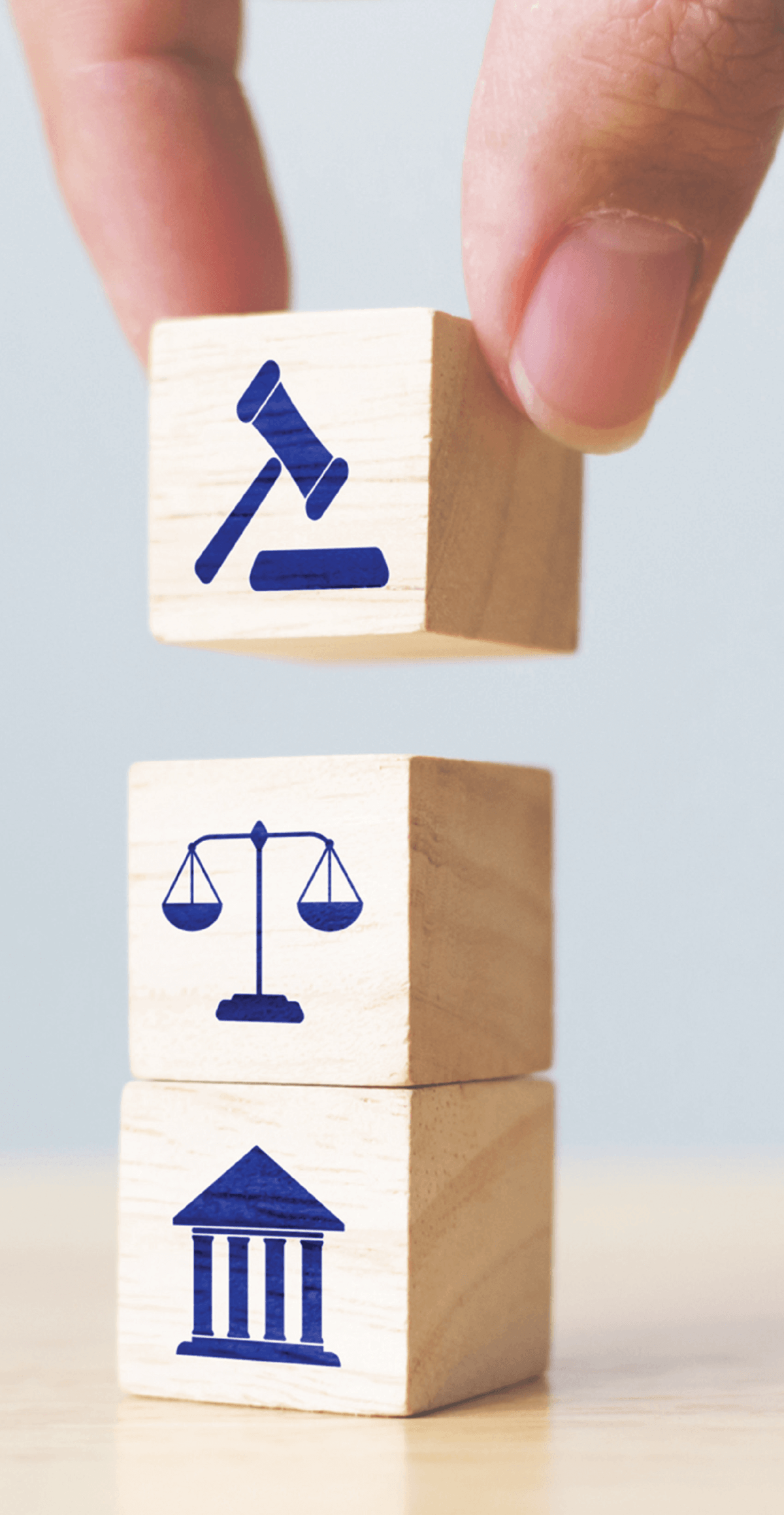 A hand placing a wooden block with a blue gavel icon atop a stack of blocks featuring scales of justice and a courthouse.