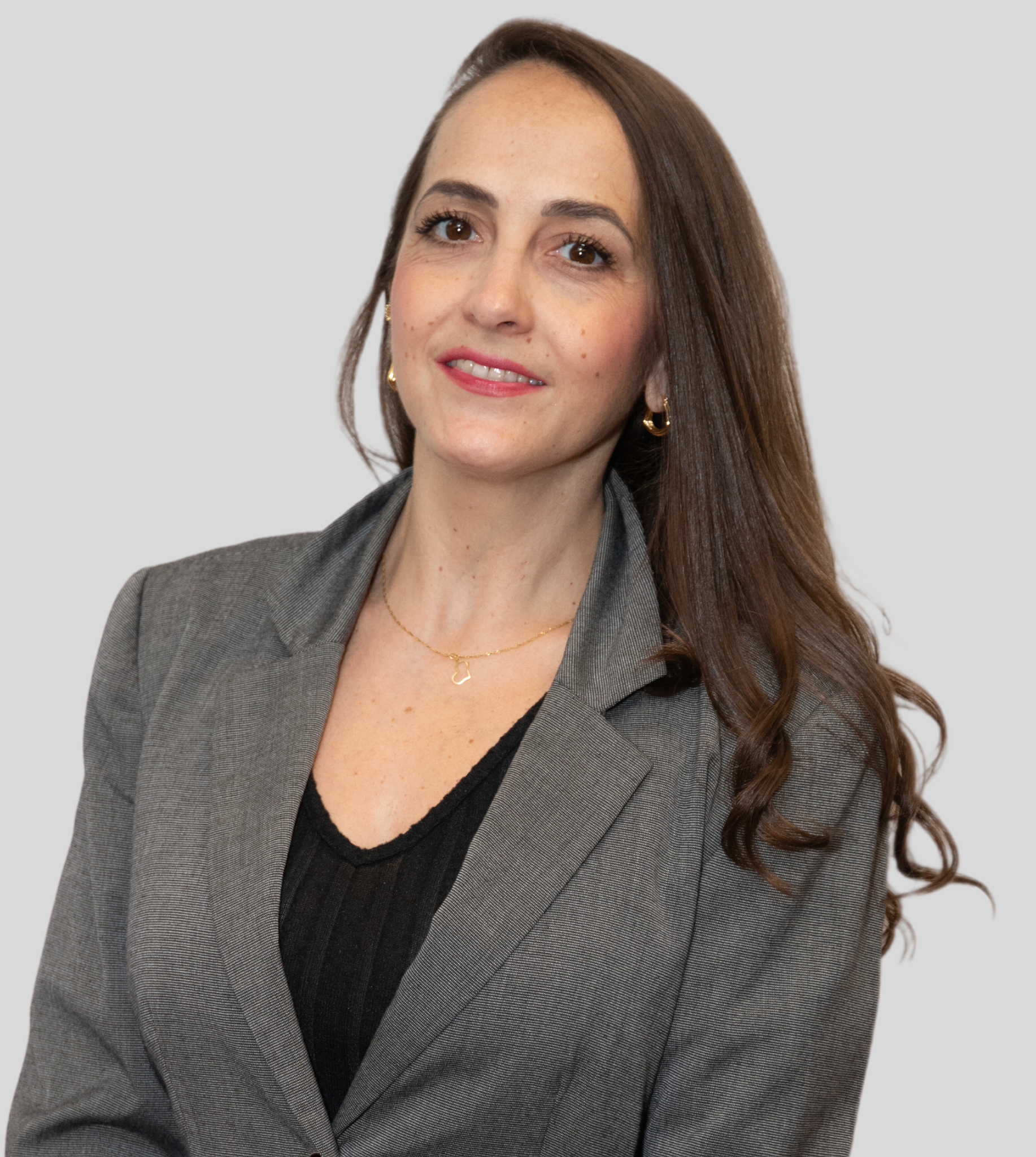 A professional headshot of a person with long brown hair, wearing a gray blazer over a black top, smiling against a gray.