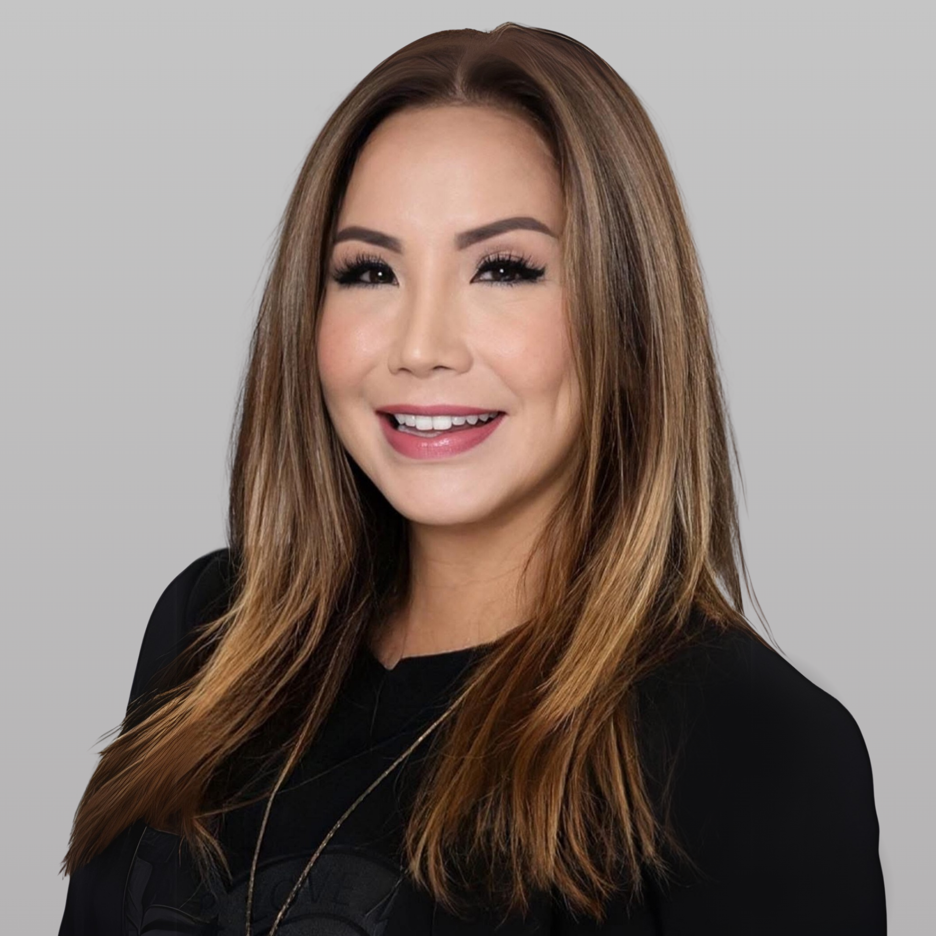 A person with shoulder-length, highlighted brown hair smiles warmly against a plain, light gray background.